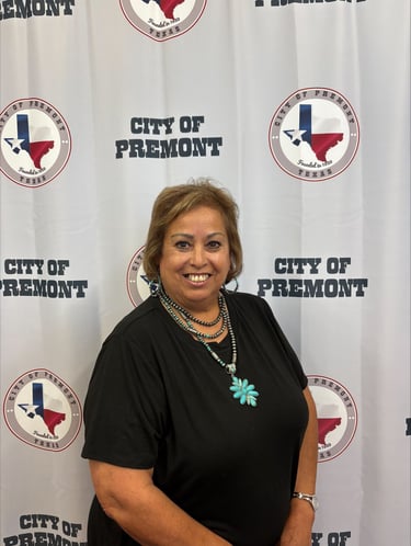 Smiling woman in black shirt and turquoise jewelry standing in front of a City of Premont Texas logo backdrop.