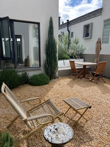 Quiet garden corner with gravel, wooden chairs, small table, white walls and simple planting for rel
