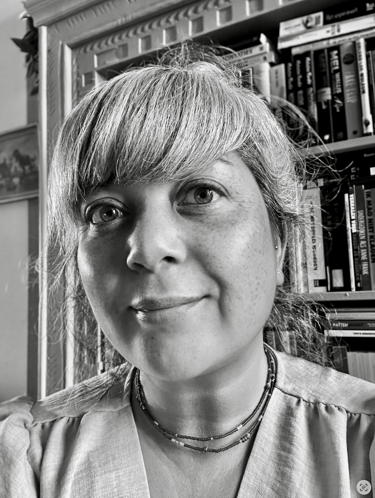 Black and white portrait of Annette in front of a bookshelf.
