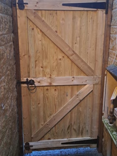 Close-up of a sturdy braced wooden side gate with black iron hinges and latch installed between two stone walls.