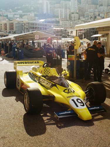 a yellow 80's Formula 1 car with a number of people standing around it