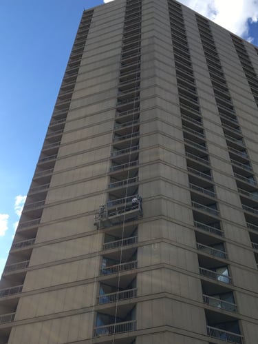 Concrete facade restoration on a tall skyscraper using a suspended work platform.