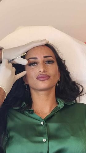 a woman in a green shirt and gloves is getting her eyebrows done