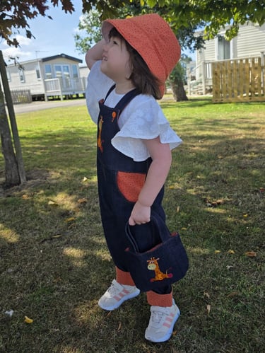 Toddler in denim giraffe dungarees and orange sun hat, made in Nottingham UK
