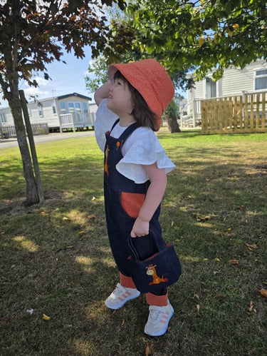 A girl wearing a sun hat and denim giraffe dungarees made in Nottingham UK 