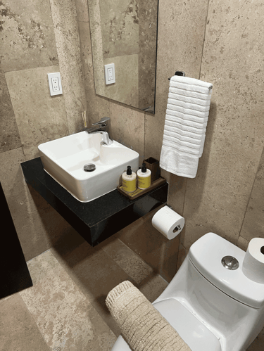 Baño con lavamanos cuadrado, espejo minimalista y recubrimiento de piedra natural beige | KARÄNA