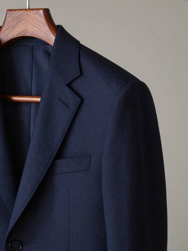 Chiaroscuro shot of a deep navy tailored suit jacket on a wooden hanger, soft side lighting highlighting structured shoulders and premium wool weave.