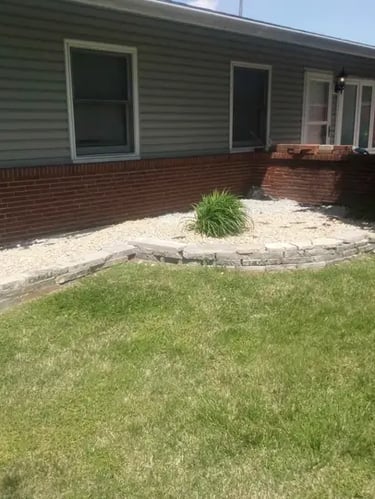 Backyard landscape featuring a tiered stone retaining wall and decorative gravel garden bed.