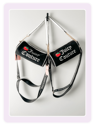 Two black Juicy Couture barrel crossbody bags with strawberry patches hanging on a wall.