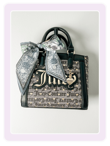 Juicy Couture monogram satchel handbag with black trim, gold hardware, and a decorative bow scarf.