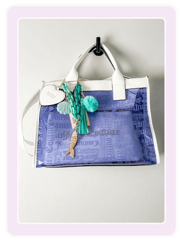 A clear Juicy Couture tote bag with purple logo interior and nautical charms.