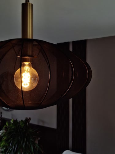 Un luminaire allumé en tissus noir devant un mur beige composé de panneaux décoratifs