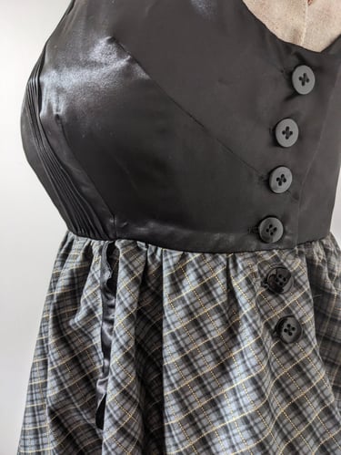 The side button closure of a black/gold plaid and black satin flowy cocktail dress