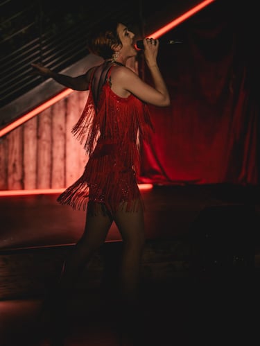 Jessie BaréKa chante sur scène en robe rouge à franges, ambiance cabaret.