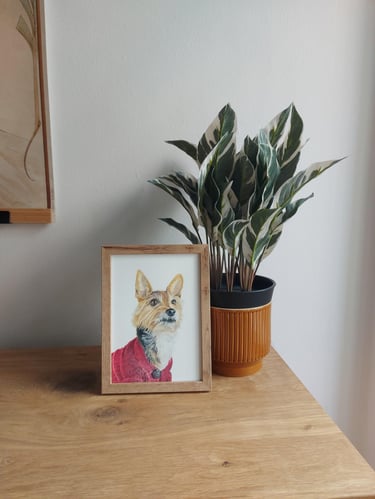 Framed A5 colored pencil dog portrait on a table next to a plant
