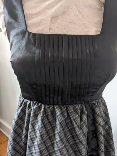 The pleated bodice of a black/gold plaid and black satin flowy cocktail dress