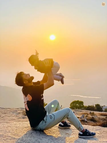 Father and daughter sharing a serene family moment during sunset at Nandi Hills, with golden light over the hills