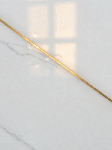 Extreme close-up of premium white alabaster marble with natural subtle grey veins, warm golden sunlight reflecting off the polished surface, editorial architectural detail.