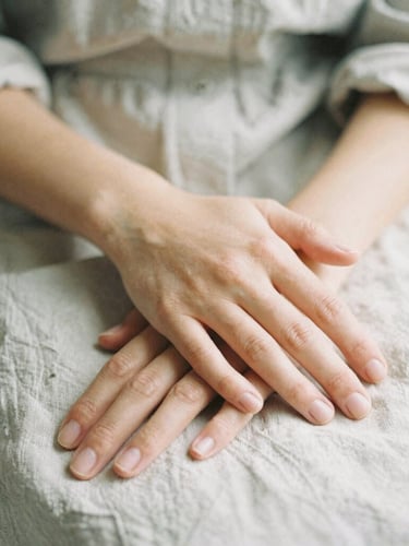 Close-up of gentle hands resting calmly over a linen shirt, soft natural light, shallow depth of field, organic and warm atmosphere