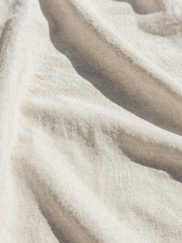 Extreme close-up of raw linen fabric texture, sun-bleached white, harsh Mediterranean midday sun casting sharp shadows, warm minimalist editorial fashion photography