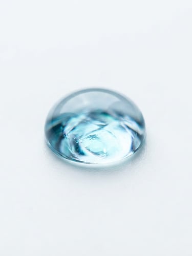 Extreme macro photograph of a sterile, clear hydrogel droplet on a pure white surface, light refracting with cool blue and teal undertones, sharp clinical focus, 85mm lens.
