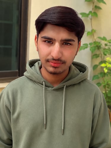 Portrait of a young man wearing a green hoodie standing outdoors near a leafy plant.