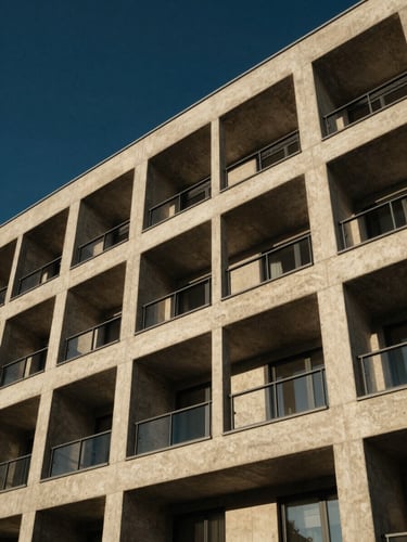 Low angle architectural photograph of a modern multi-family concrete and steel building structure, crisp morning sunlight casting sharp shadows, deep navy sky background, 35mm lens.