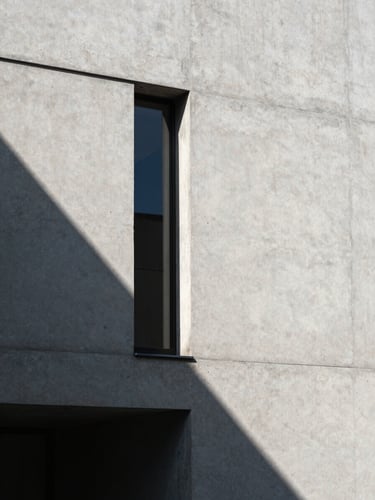 Sharp architectural detail of a concrete minimalist building facade, casting a stark geometric shadow under direct sunlight.