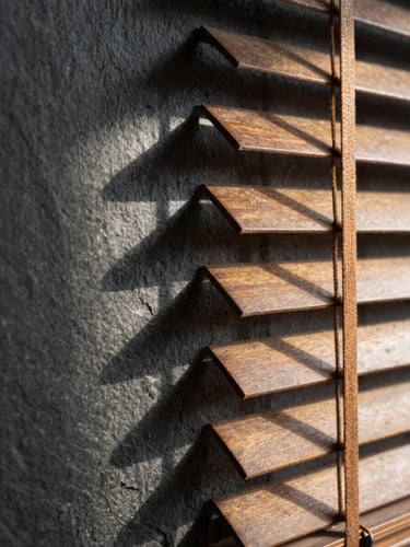 Macro close-up of warm afternoon light filtering through wooden blinds onto a dark slate wall, casting long architectural shadows, quiet library atmosphere.