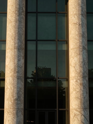 Editorial architectural close-up of a luxury concrete and glass facade, warm golden-hour sunlight reflecting on premium marble columns, symmetrical framing, 35mm