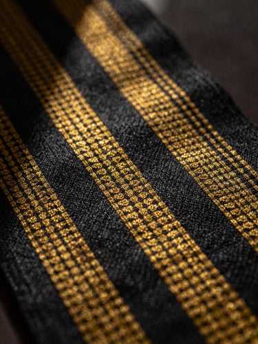 Extreme macro chiaroscuro shot of authentic handwoven Alindi cloth, sharp geometric patterns in gold and obsidian threads, dramatic side lighting