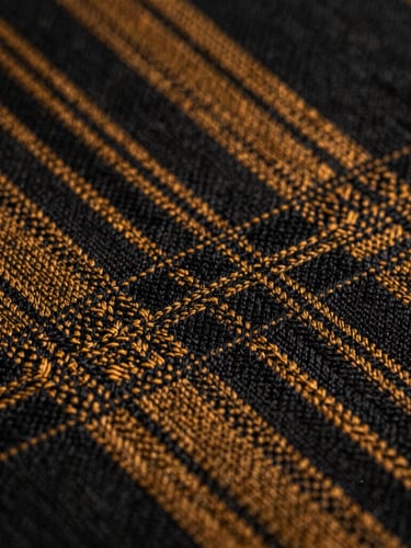 Extreme close-up macro shot of authentic Alindi cloth showing sharp geometric weaving patterns of black and deep amber threads under high-contrast chiaroscuro lighting.