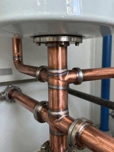 Close-up of clean copper welds and neat piping on a newly installed high-efficiency boiler system, bright basement work-light, 35mm lens