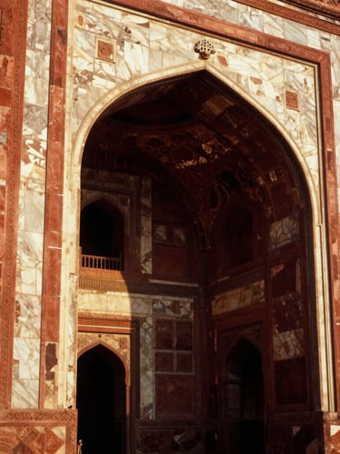 Close-up of intricate Mughal carvings on a red sandstone archway, dramatic side-lighting from the low golden sun casting deep shadows, 35mm film style.