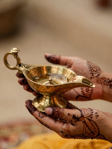 Close-up of hands decorated with intricate henna holding a ceremonial brass lamp, soft warm lighting, shallow depth of field.