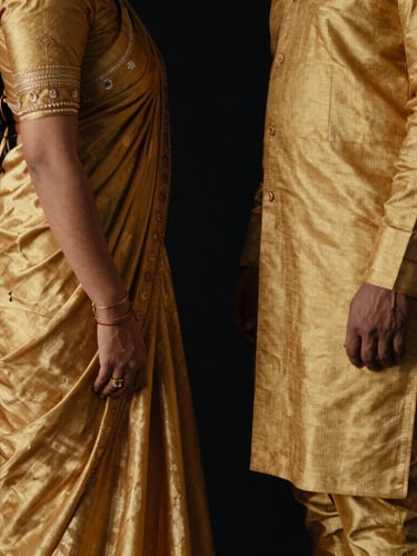 Low-key cinematic fashion photography of a sophisticated Assamese couple in structured golden Muga silk garments, high-contrast shadows, matte black backdrop, medium format film.