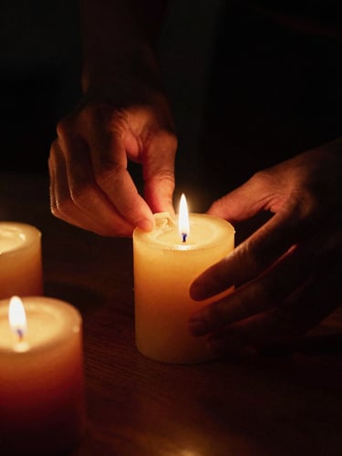 Close-up of hands preparing a beeswax candle, dark chiaroscuro lighting with warm golden candlelight casting long shadows, rich gold and crimson tones, 35mm film grain