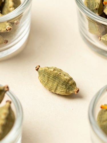 Macro top-down shot of whole, unbroken green cardamoms and golden saffron threads in elegant glass vessels, soft natural daylight, minimalist styling