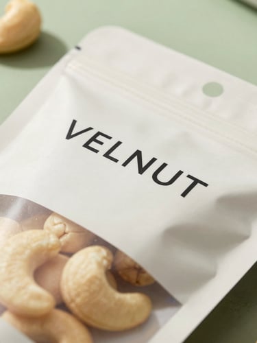 Close-up of premium minimalist packaging for VELNUT, showcasing clean labels and pristine cashews inside, soft natural daylight, sage green backdrop.