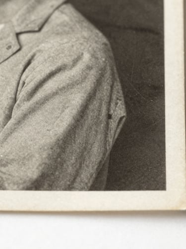 Macro photograph of a vintage 1940s black and white photograph edge, showing silver halide emulsion texture and paper fibers under soft side-lighting, archival museum style.