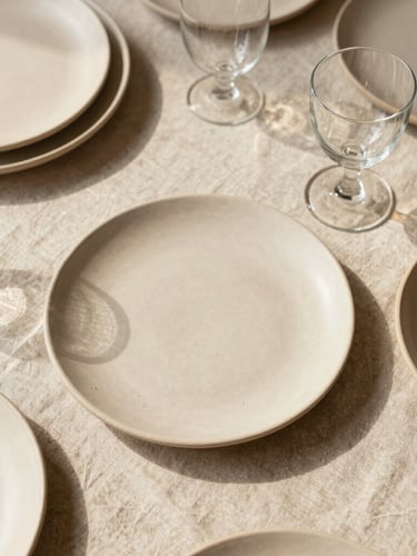 Overhead flat-lay of a curated tablescape with natural linen, hand-thrown ceramic plates, and delicate glassware bathed in soft afternoon daylight, warm wheat beige tones