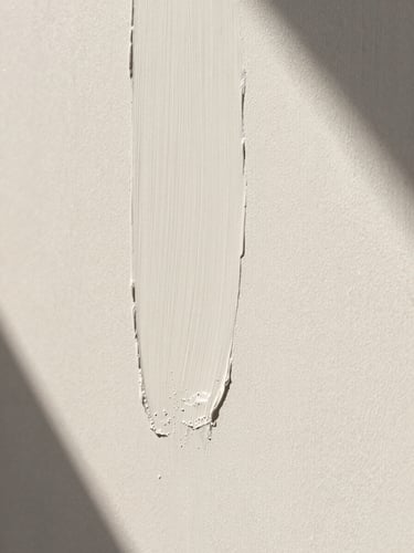 Extreme close-up of a hand-applied lime wash wall texture, warm chalky white color, soft natural side light casting delicate shadows, architectural minimalism.