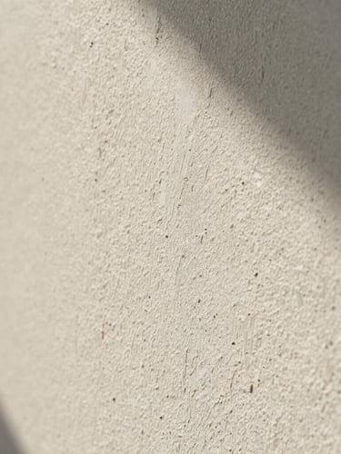 Macro close-up of a warm chalky white lime wash plaster wall, catching soft morning sunlight with delicate natural shadows, highly detailed mineral texture.