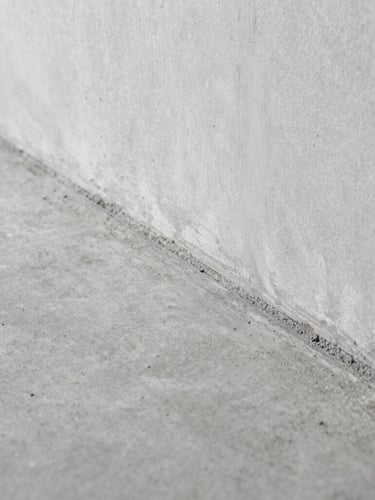 Macro side-lit architectural photograph showing a perfectly level concrete subfloor meeting a clean wall plate, highlighting the smooth leveled surface texture