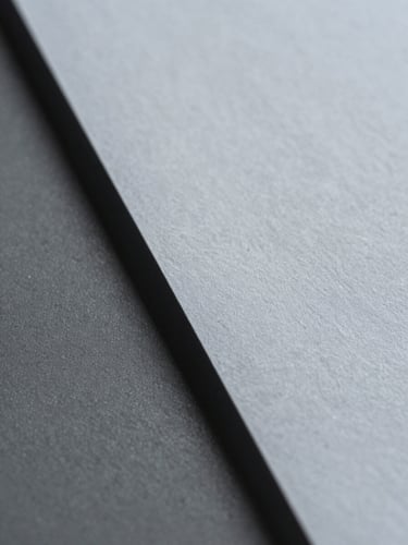Extreme macro close-up of heavy cotton document paper with embossed texture, sharp architectural shadow cutting diagonally, cool grey tones