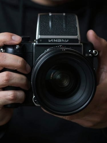 Photographer's hands adjusting a medium-format camera lens, extreme close-up, high-contrast studio lighting, sharp focus on the tactile details of the lens and fingers, deep blacks, cool grays.