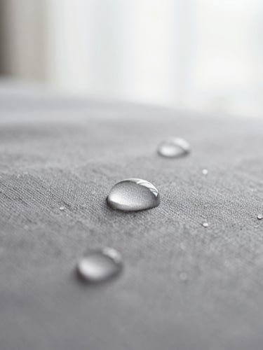 Macro detail shot of water droplets beading on a textured grey fabric surface, shallow depth of field, soft diffused morning light
