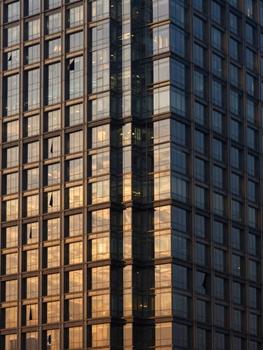 Symmetrical architectural photography of a modern high-rise commercial tower in Gurgaon, golden-hour window light reflecting off glass facade, deep navy tones, sharp details, 35mm