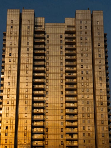 Symmetrical golden-hour architectural twilight shot of a luxury high-rise tower in Gurgaon, deep navy sky, warm gold lights reflecting off modern glass facade, 35mm premium photography