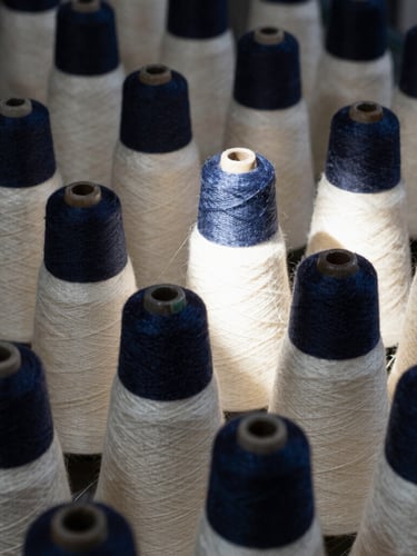Macro shot of wound cones of silk yarn on a spinning spindle, high-contrast industrial shadows, natural light, deep navy tones